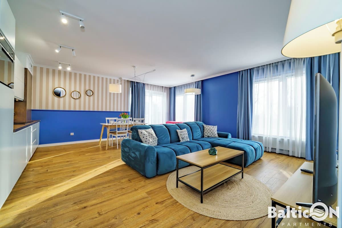 Ein modernes Wohnzimmer mit einem blauen Sofa, Holzböden und einem Essbereich mit Tisch und Stühlen.