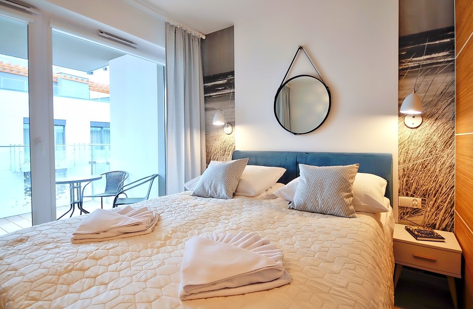 Una habitación de hotel con una cama grande, un espejo redondo, una mesita de noche y vistas al balcón exterior.