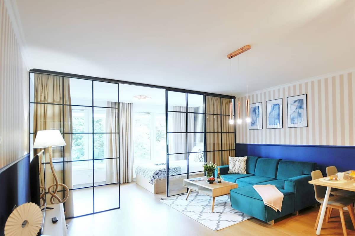 Ein modernes Wohnzimmer mit Sofa, Couchtisch und Esstisch. Große Fenster mit Vorhängen, eine Lampe und Kunstwerke an der Wand.