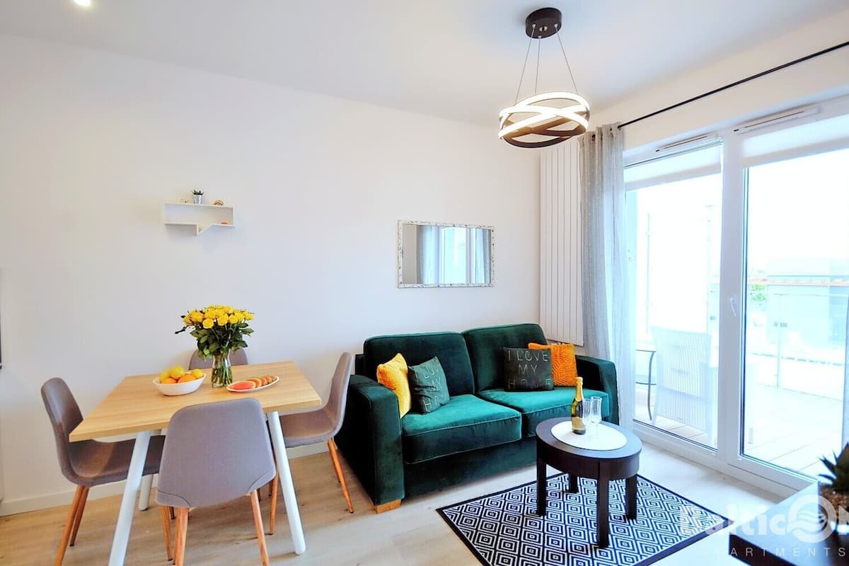 Ein modernes Wohnzimmer mit einem grünen Sofa, einem Esstisch mit Stühlen, einem kleinen Couchtisch und einem großen Fenster mit Vorhängen.