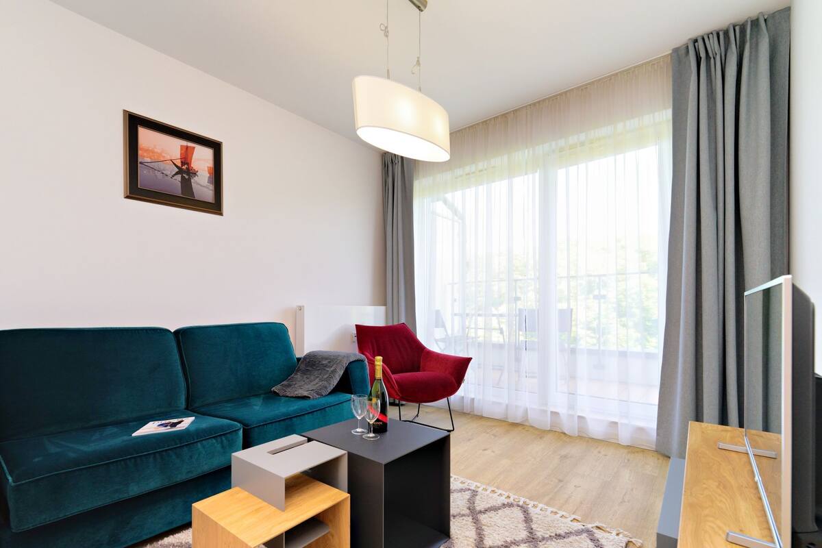 Ein modernes Wohnzimmer mit einem türkisfarbenen Sofa, einem roten Sessel, einem kleinen Holztisch und einem gerahmten Bild an der Wand.