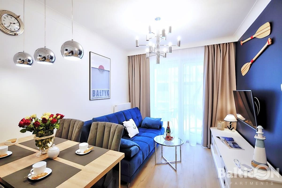 Ein modernes Wohnzimmer mit einem blauen Sofa, einem Esstisch mit Blumenvase, einer Kristallleuchtre und einer Wanduhr.