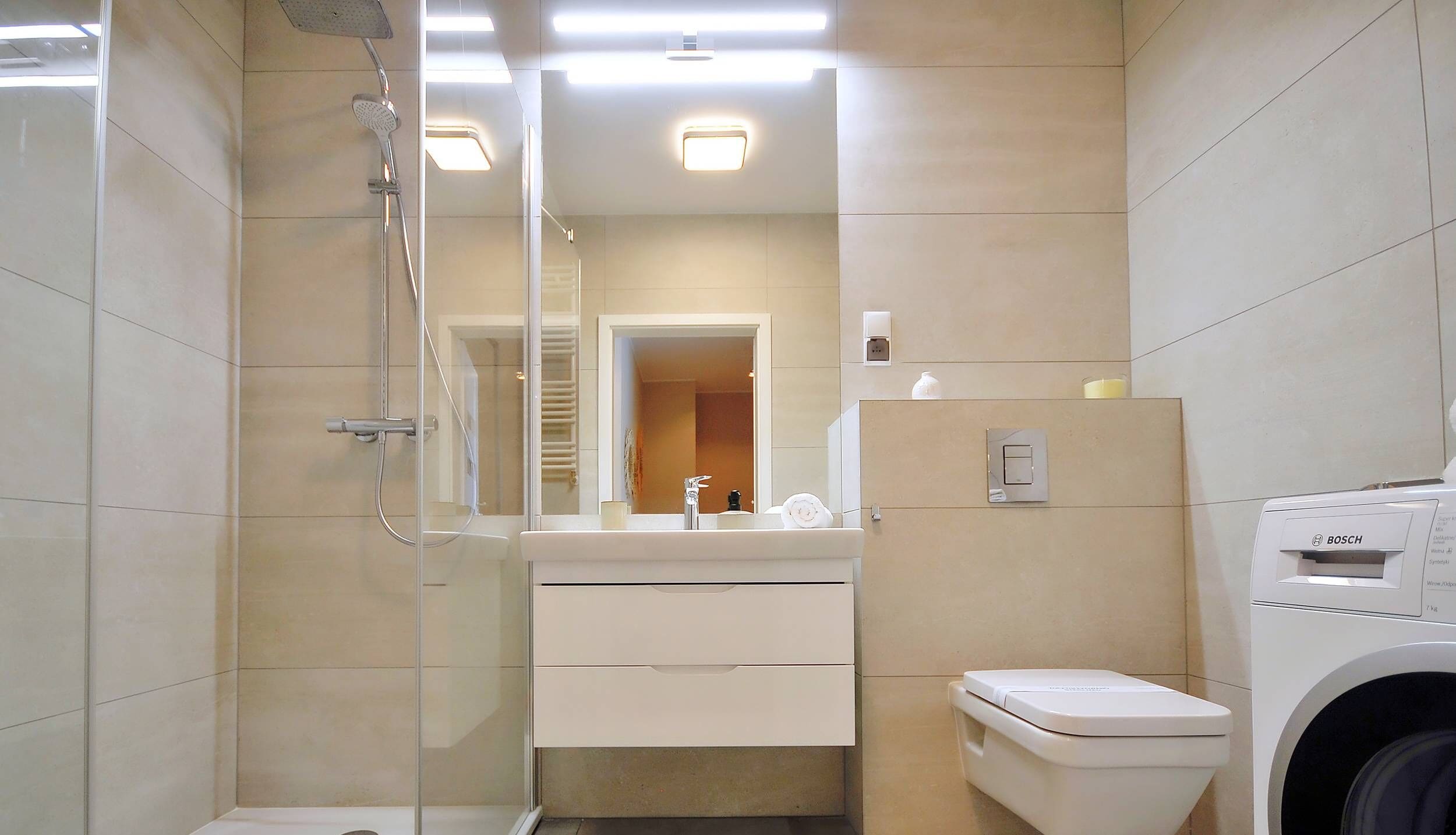 Une salle de bain moderne avec une douche à parois de verre, des toilettes, un lavabo avec un miroir et un lave-linge Bosch.