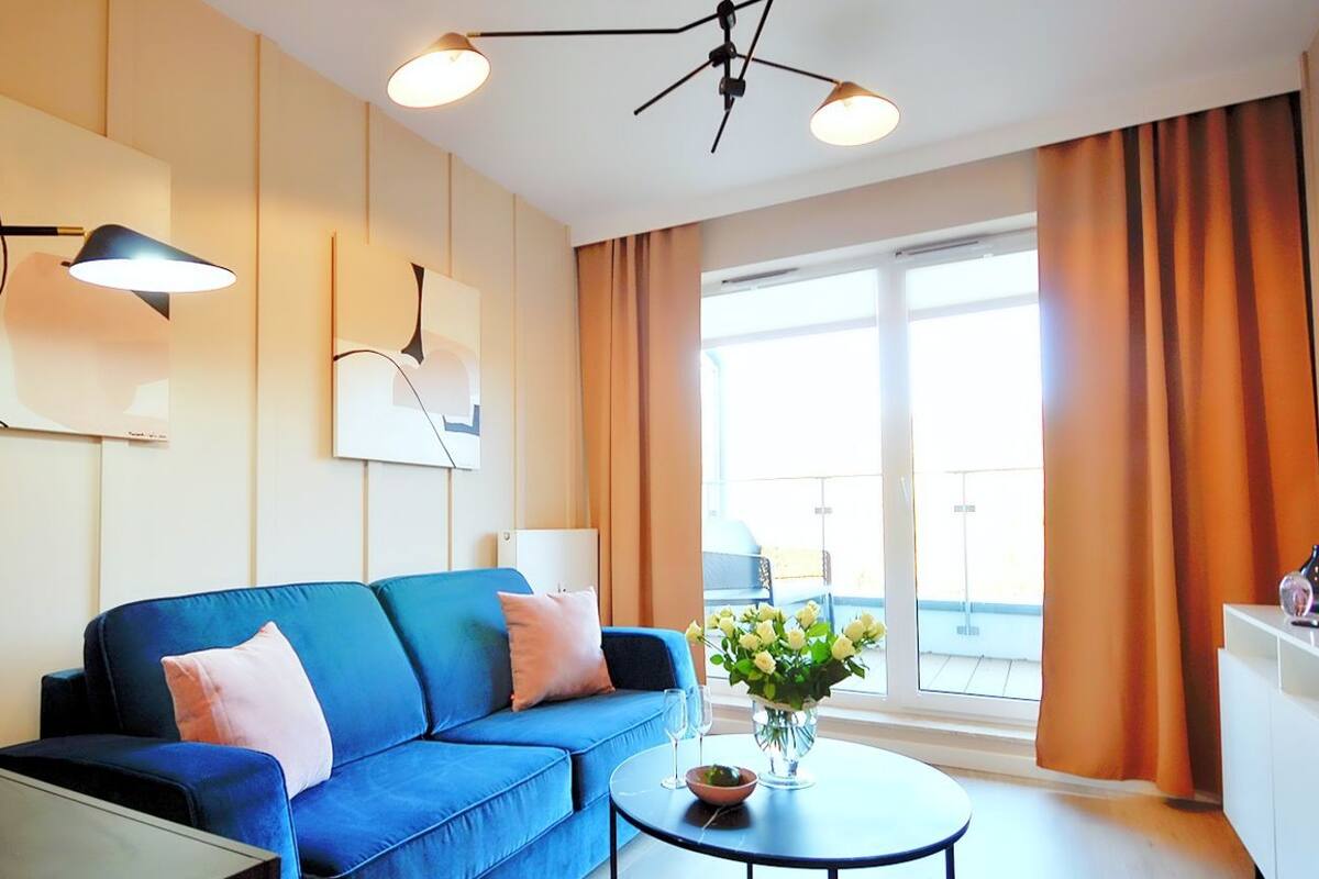 Ein modernes Wohnzimmer mit einem blauen Sofa, einem runden Couchtisch und einem großen Fenster mit Vorhängen.