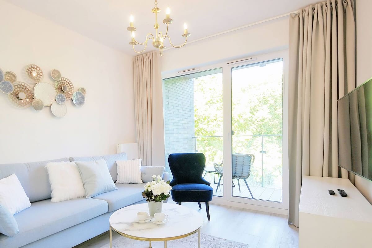 Ein modernes Wohnzimmer mit einem hellblauen Sofa, einem dunkelblauen Sessel, einem runden Couchtisch und einer Kristallleuchtre.