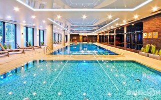 En modern inomhuspool med klart vatten, omgiven av solstolar och ett väl upplyst tak med stjärnliknande lampor.