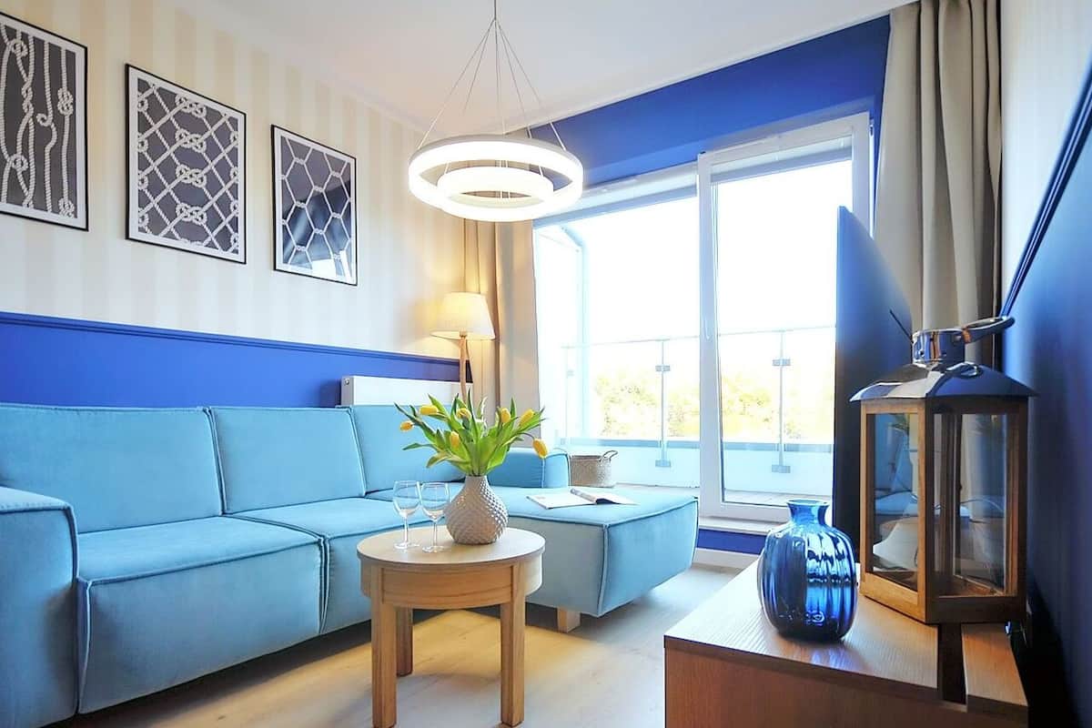 Ein Wohnzimmer mit einem blauen Sofa, einem runden Holztisch mit einer Vase und einer Stehlampe.