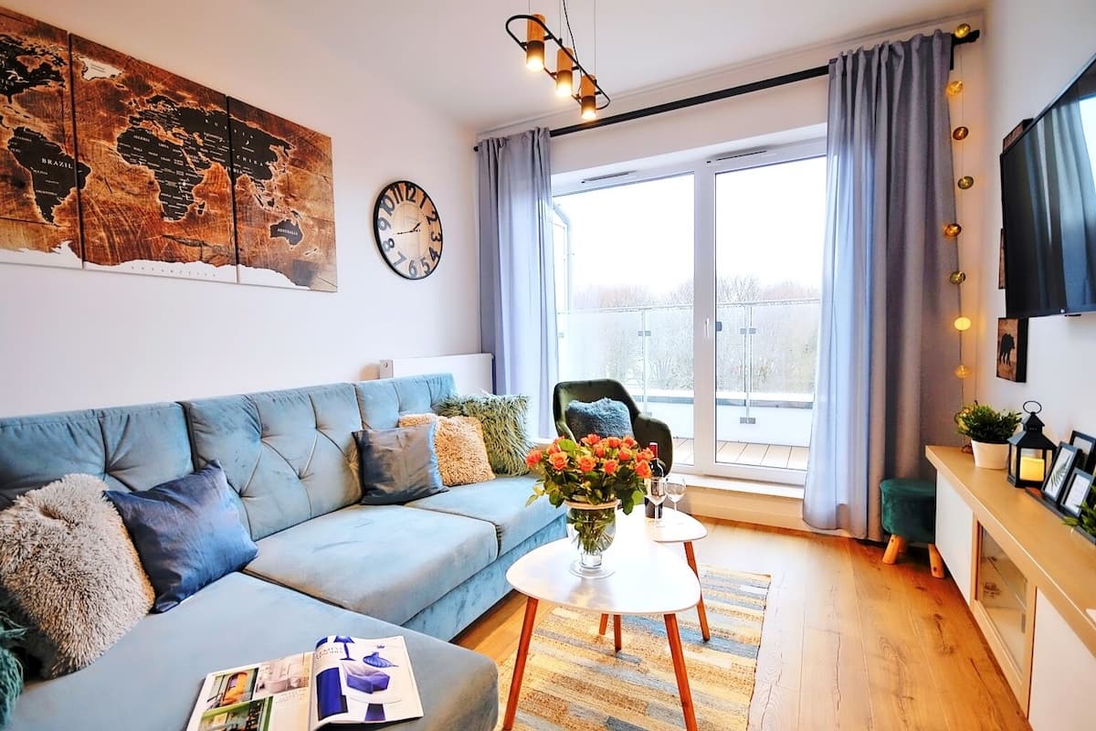 Ein modernes Wohnzimmer mit einem blauen Sofa, einer Weltkarte, einer Uhr und einem Balkon mit Blick.