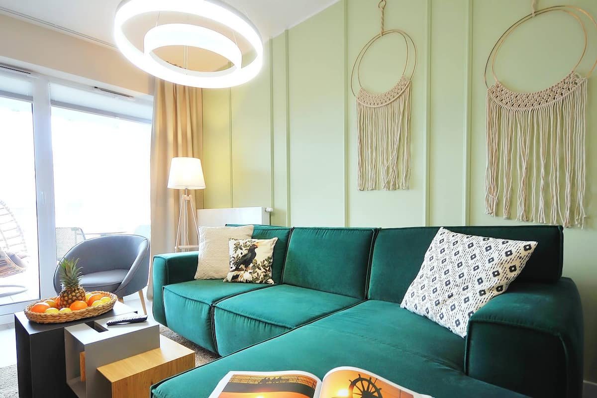 Ein modernes Wohnzimmer mit einem grünen Sofa, einem kleinen Beistelltisch mit einer Fruchtkorb und einer Wanddekoration aus Makramee.