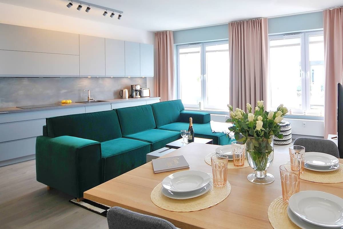 Eine moderne Küche mit grauen Schränken, einem türkisgrünen Sofa und einem Essbereich mit einem Holztisch für vier Personen.