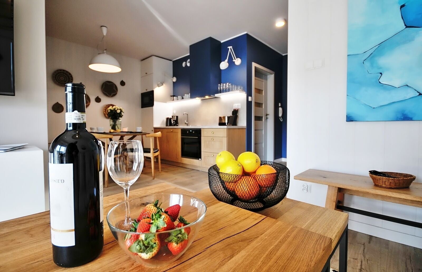 Una cocina moderna con una mesa de comedor dispuesta, una botella de vino, copas y un frutero.