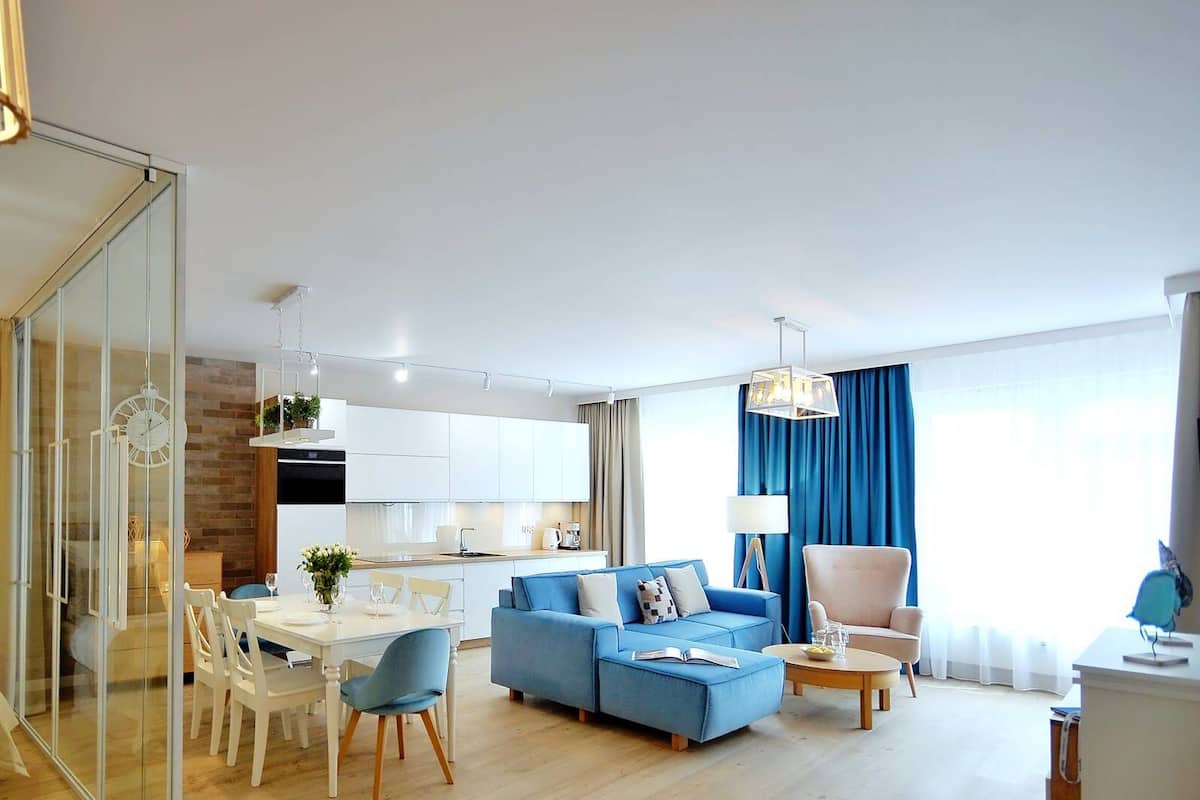 Ein modernes Wohnzimmer mit einem blauen Sofa, einem Esstisch und einer Küche im Hintergrund.