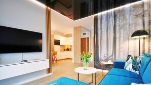 A modern living room with a flat-screen TV, a blue sofa, and a coffee table with a vase of flowers. - BalticON Nadmorskie Tarasy (Kolobrzeg)