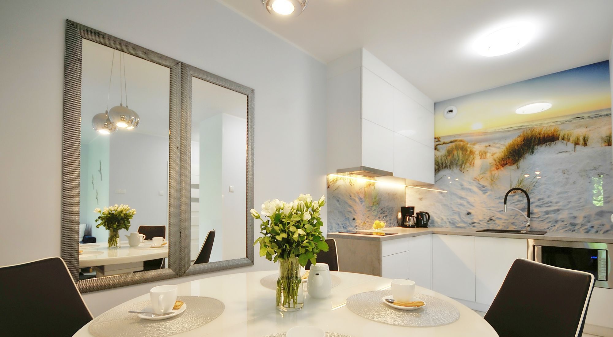 A modern dining area with a round table, chairs, a vase with flowers, and a large mirror.