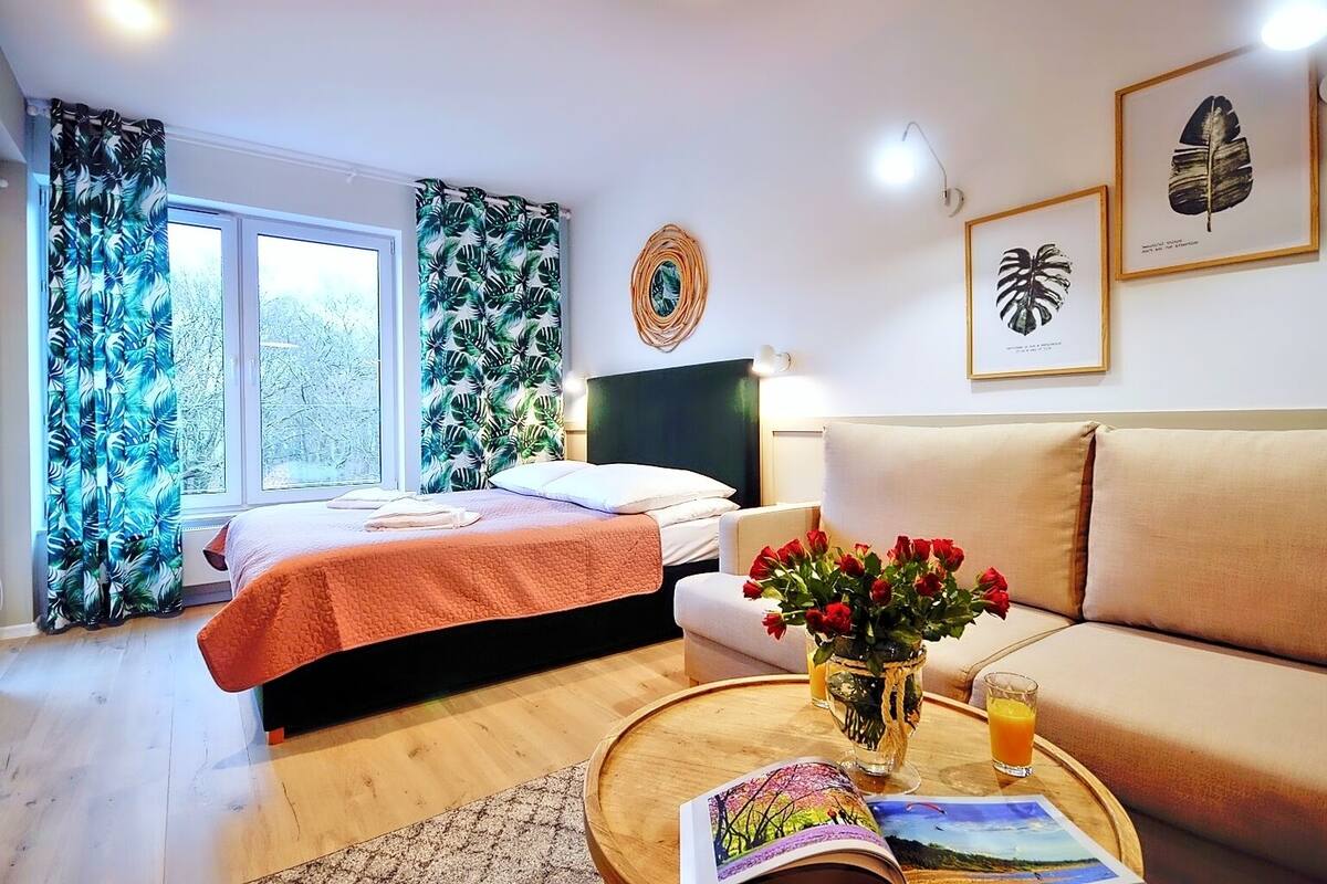 Ein Zimmer mit einem Bett, einer Couch, einem kleinen Tisch mit Blumenvase und einem gerahmten Bild an der Wand.