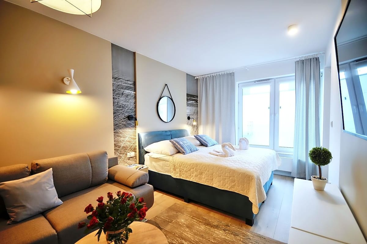 Ein modernes Schlafzimmer mit Bett, Sofa, Spiegel und einem Blumentopf.