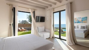 Een slaapkamer met een bed, een televisie, een balkon met zwembad en uitzicht op zee.
