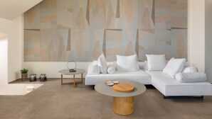 Een moderne woonkamer met een hoekbank, een ronde salontafel en een geometrisch kunstwerk aan de muur.