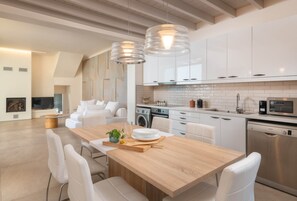 A modern kitchen with white cabinets, stainless steel appliances, and a wooden dining table with white chairs.