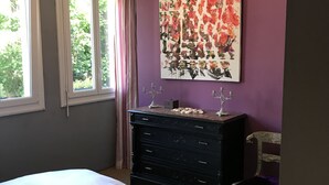 A bedroom with a bed, dresser, and a large floral painting on the wall. - Very bright F2 with terrace and panoramic view of the Port <br> (Sète)