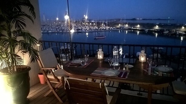 A table set for two with a view of a marina at dusk. - Very bright F2 with terrace and panoramic view of the Port <br> (Sète)