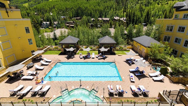 Et resort med en central pool, liggestole og udsigt til en skovklædt bakke.