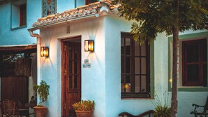 Un edificio tradicional con puerta de madera, dos macetas y un banco en el exterior.