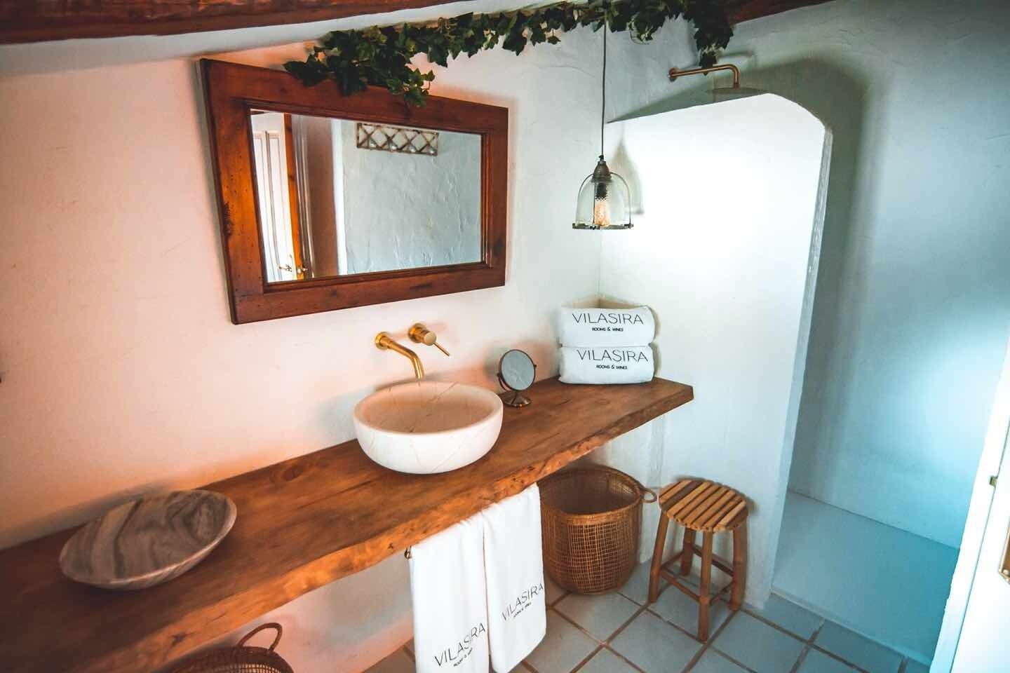 Un baño con tocador de madera, un lavabo redondo, un espejo, una lámpara colgante y un cartel que dice "VILASIRA".