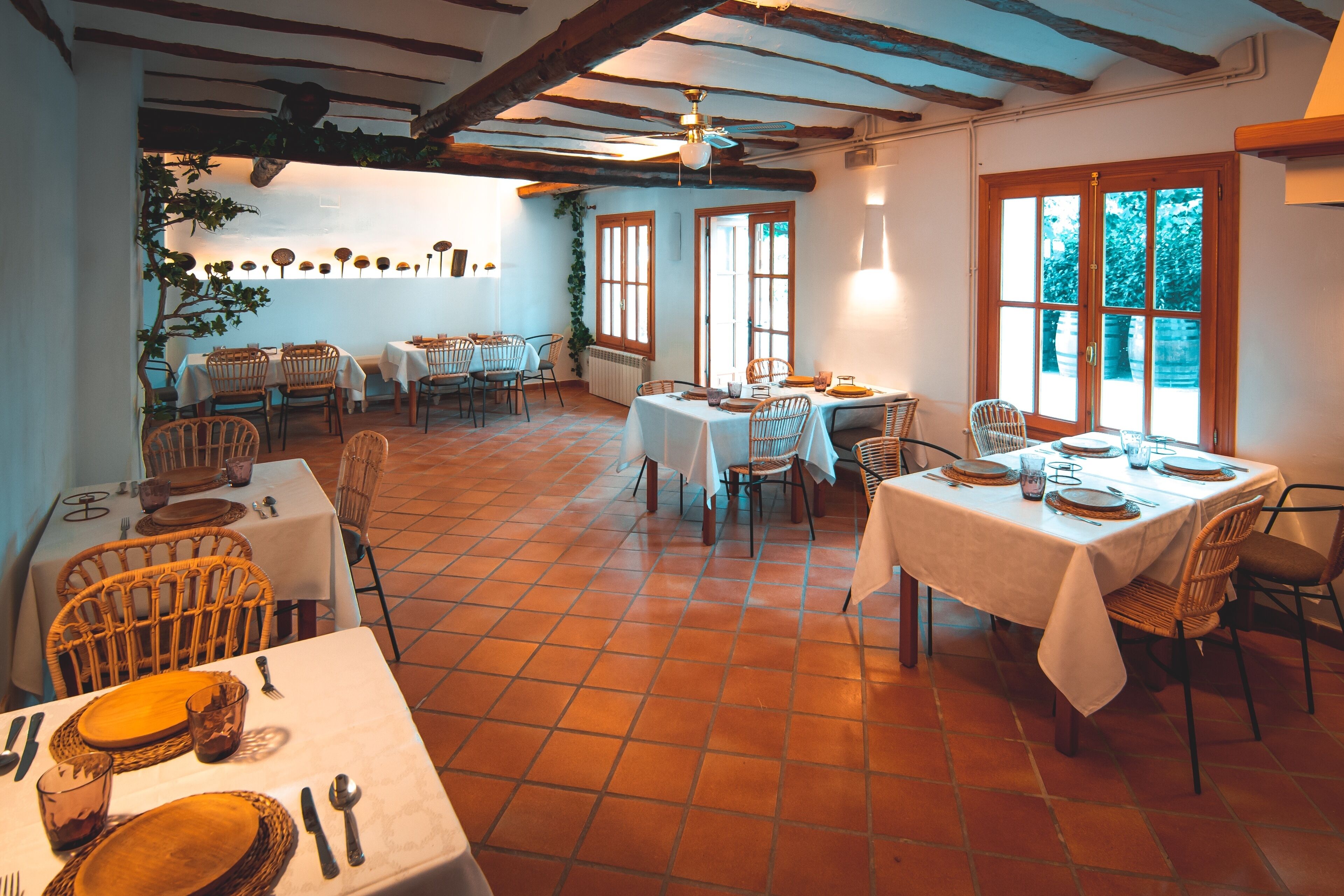 Comedor con varias mesas dispuestas para comidas, con sillas de mimbre y manteles blancos.