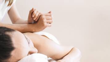 Nært billede af en massage, hvor fokus er på hænderne og en persons ryg.
