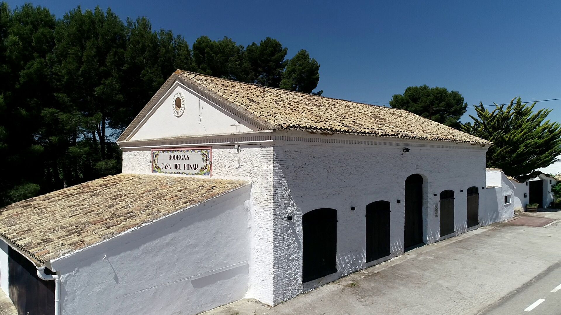 A white building with a tiled roof and a sign reading "BODEGAS CASA DEL PINAR".