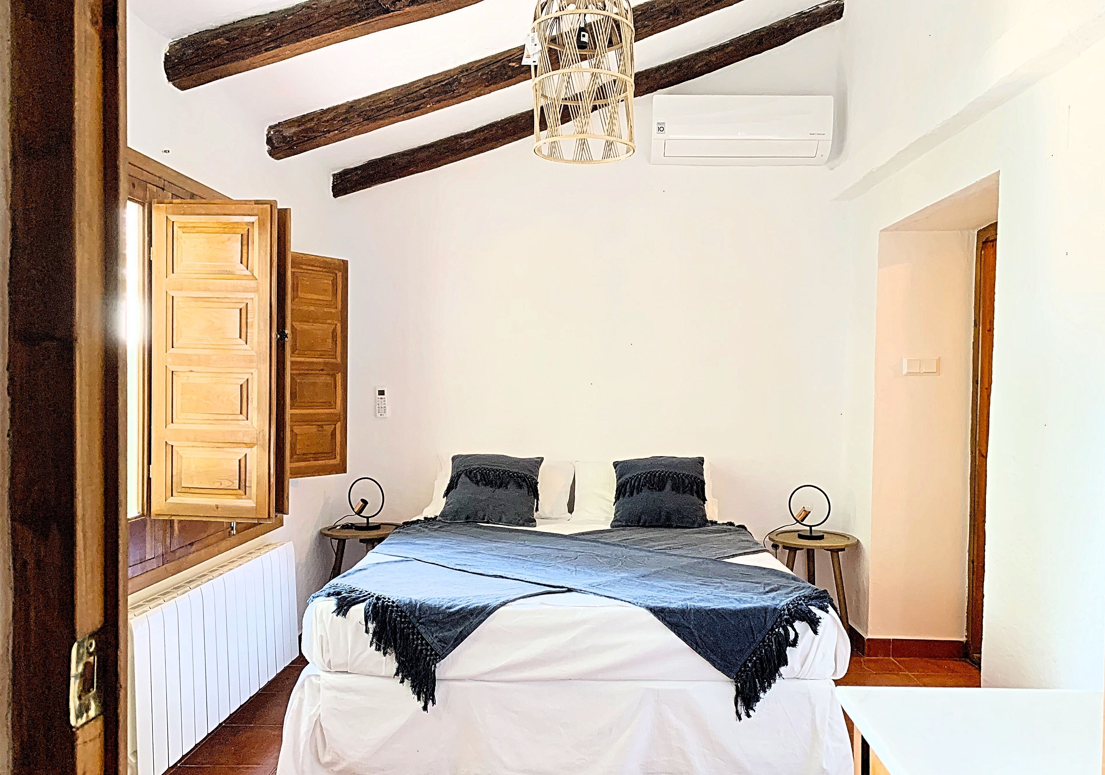 Un dormitorio con una cama, dos mesitas de noche, una lámpara colgante y vigas de madera en el techo.
