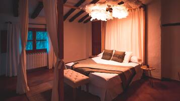 Un dormitorio con cama a dosel, un banco, una mesita y vistas a una ventana con cortinas.