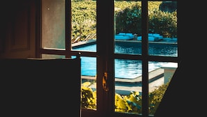 Vista a través de una ventana de un área de piscina con sillas de descanso.