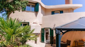 Un edificio moderno con fachada curva, un área de estar exterior cubierta y una puerta que da a una habitación.