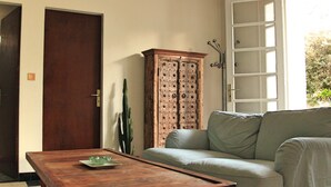 A room with a checkered floor, a wooden table, a green sofa, a wooden cabinet, and a hanging light fixture. - Villa Suzanne terrace and veranda near the beach (Longeville-sur-Mer)