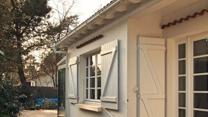 A wooden deck leading to a white building with a tiled roof, a sliding glass door, and a window with shutters. - Villa Suzanne terrace and veranda near the beach (Longeville-sur-Mer)