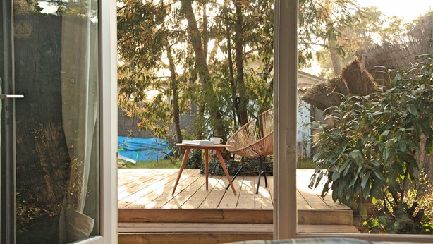 A wooden deck with a chair and a table, surrounded by trees and a blue tarp. - Villa Suzanne terrace and veranda near the beach (Longeville-sur-Mer)