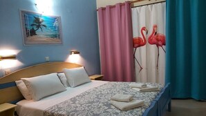 A hotel room with a bed, two bedside tables, a nightstand, a painting of a beach scene, and curtains with flamingo designs. - Flamingo Apartments by CorfuEscapes (Corfu)