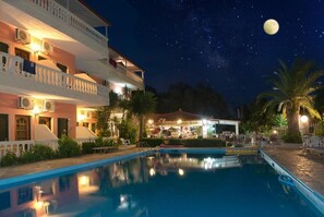A nighttime view of a hotel with a swimming pool, a bar, and a moon in the sky.