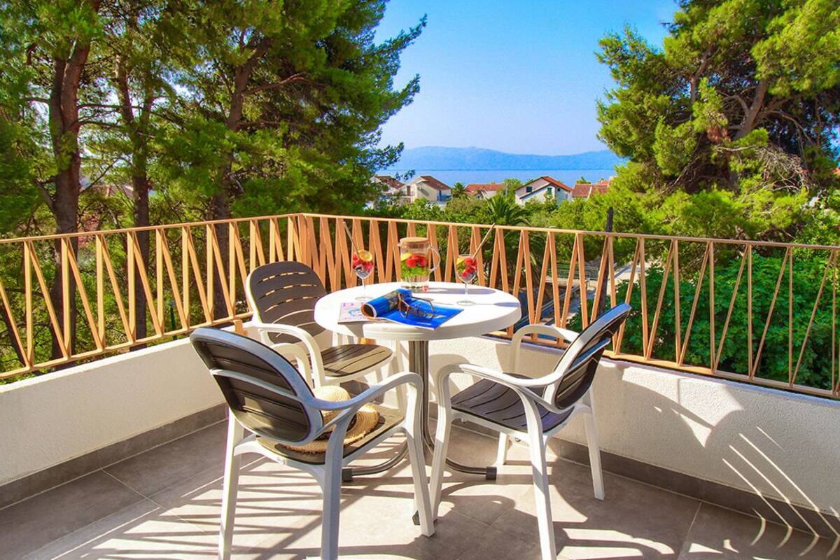 A balcony with a table and chairs, overlooking a scenic view of trees and a distant coastline.