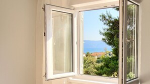 Finestra aperta con vista su un paesaggio costiero e alberi.