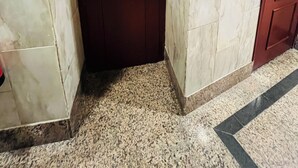 A corner of a room with a dark wooden door, white tiled walls, and a granite floor. - Pension Rivera (Madrid)