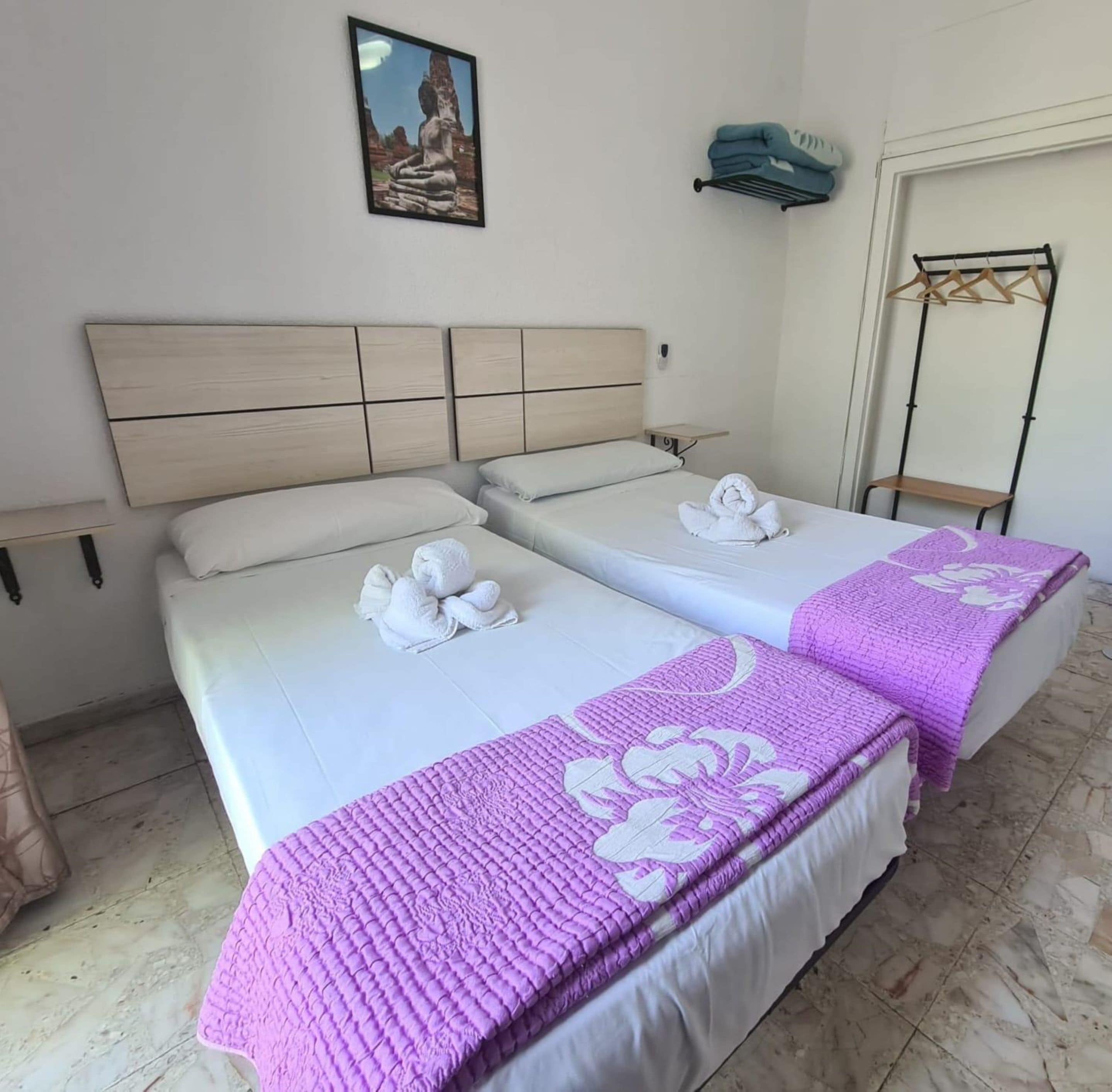 A hotel room with two beds, a headboard, a wall-mounted picture, a towel rack, and a mirror.