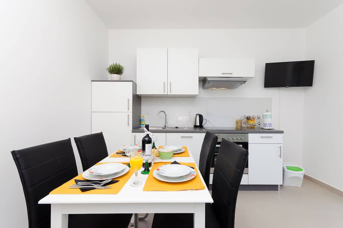 A modern kitchen with white cabinets, a flat-screen TV mounted above the counter, and a dining area with a table set for two.