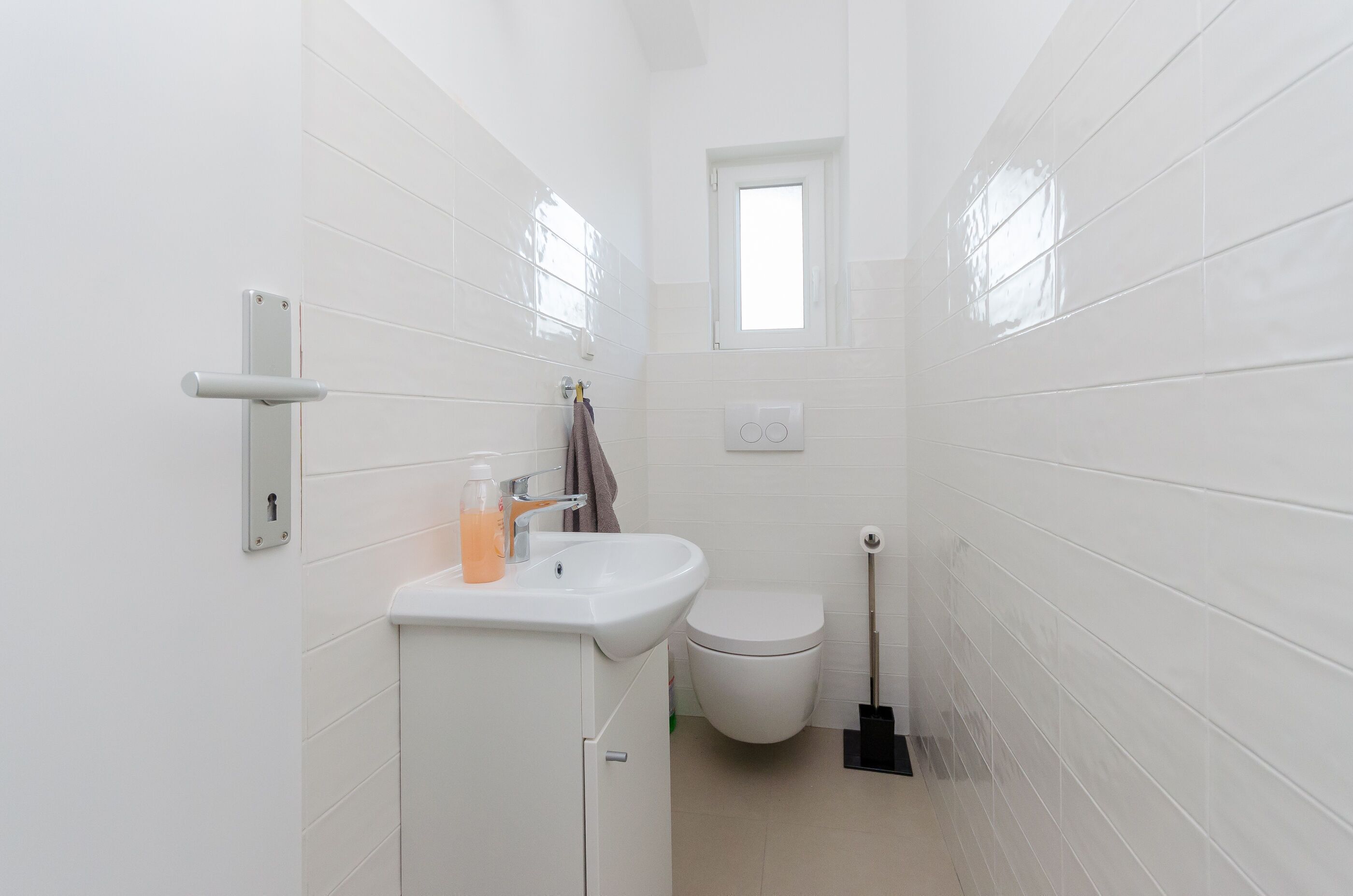 Un baño pequeño y blanco con inodoro, lavamanos y ventana.