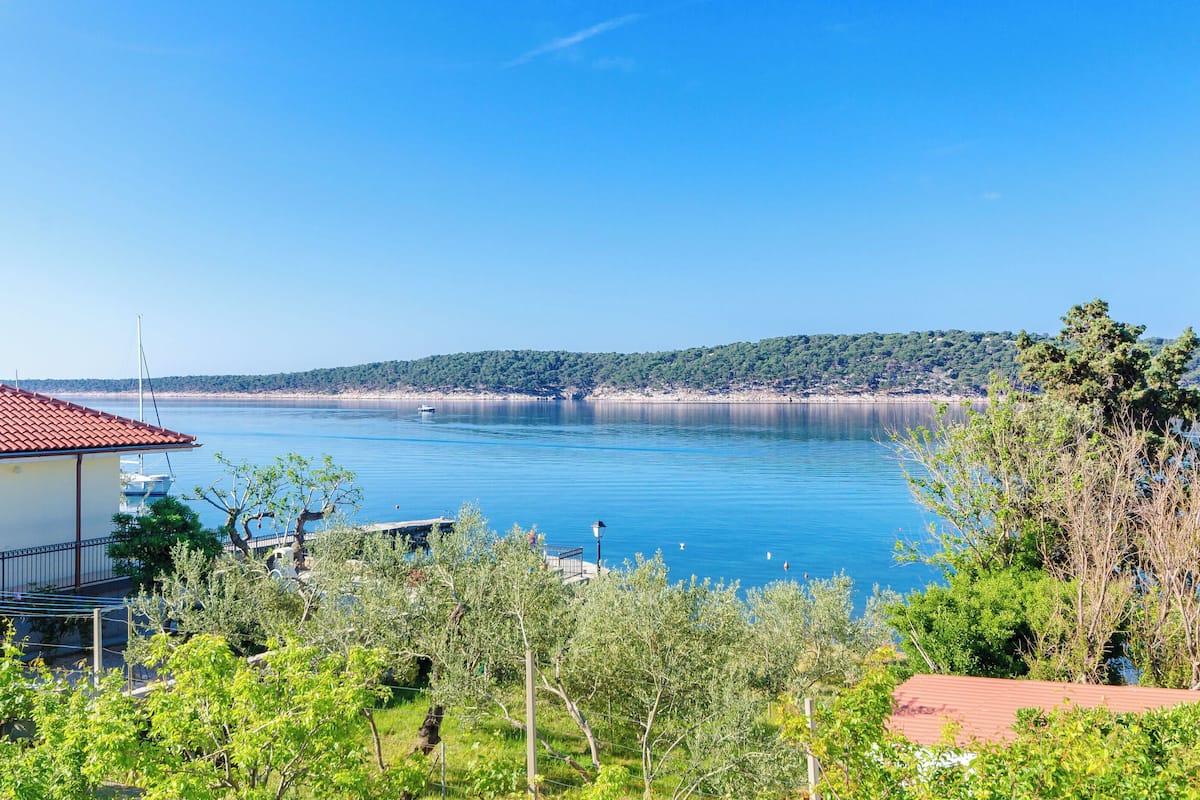A coastal view with a clear sky, a calm sea, and a distant tree-covered hill.