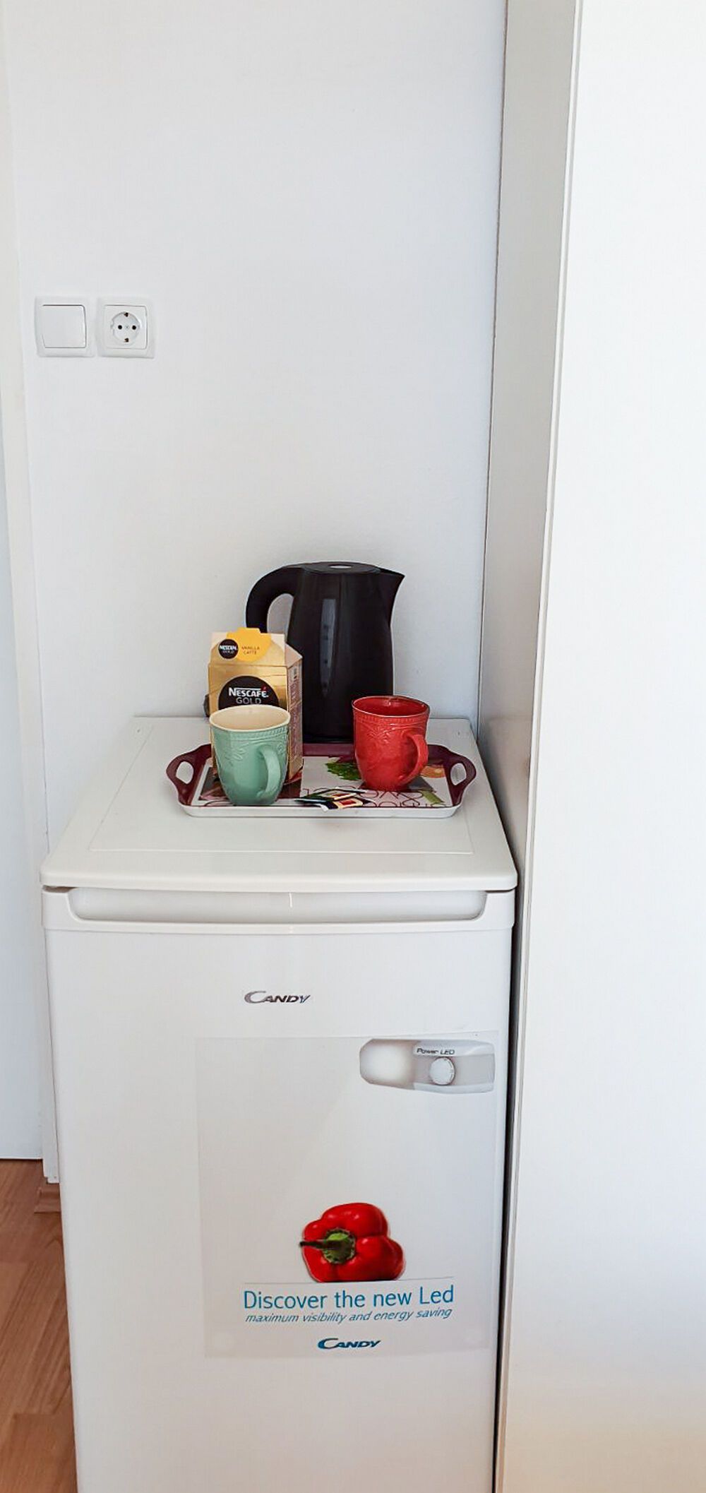 A white mini-fridge with a Nescafe Gold coffee pod, a red mug, and a green mug on top.