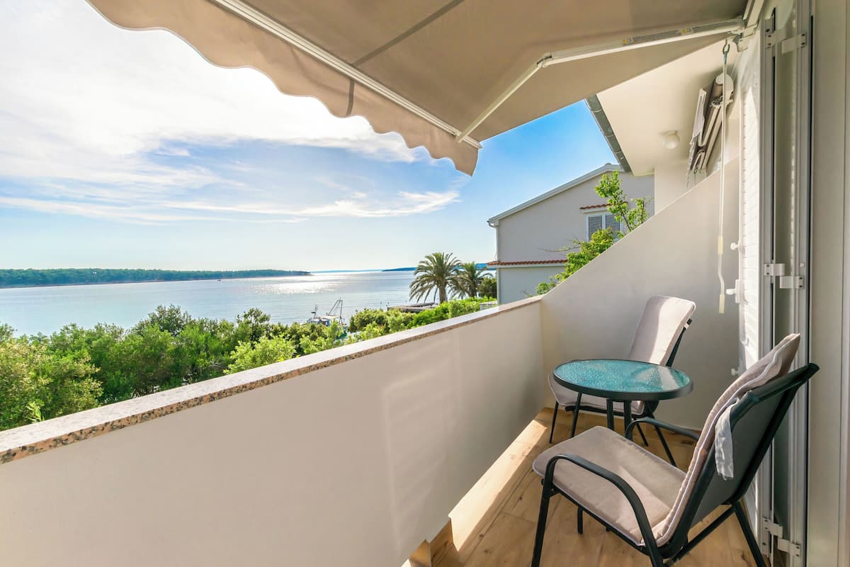 A balcony with a view of the sea, a table, and two chairs.