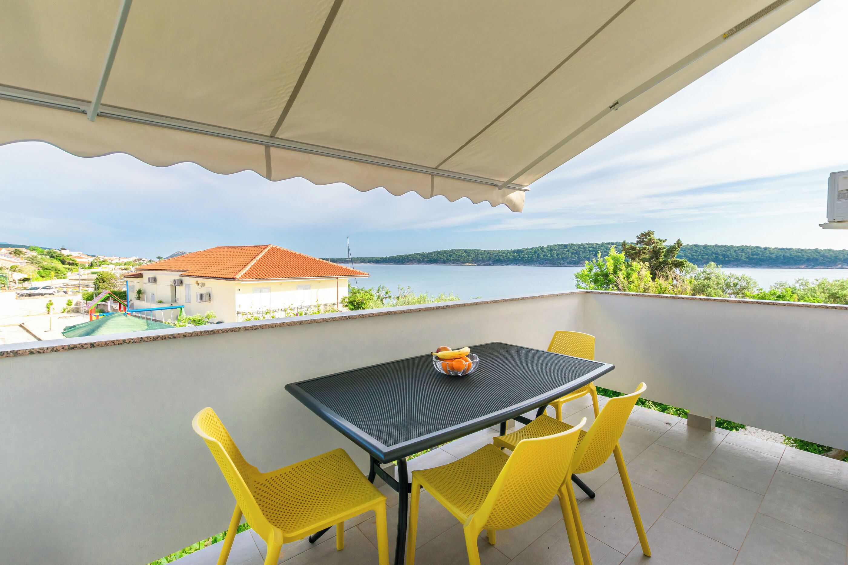 Un balcon avec une table et des chaises, donnant sur une étendue d’eau et un paysage lointain.